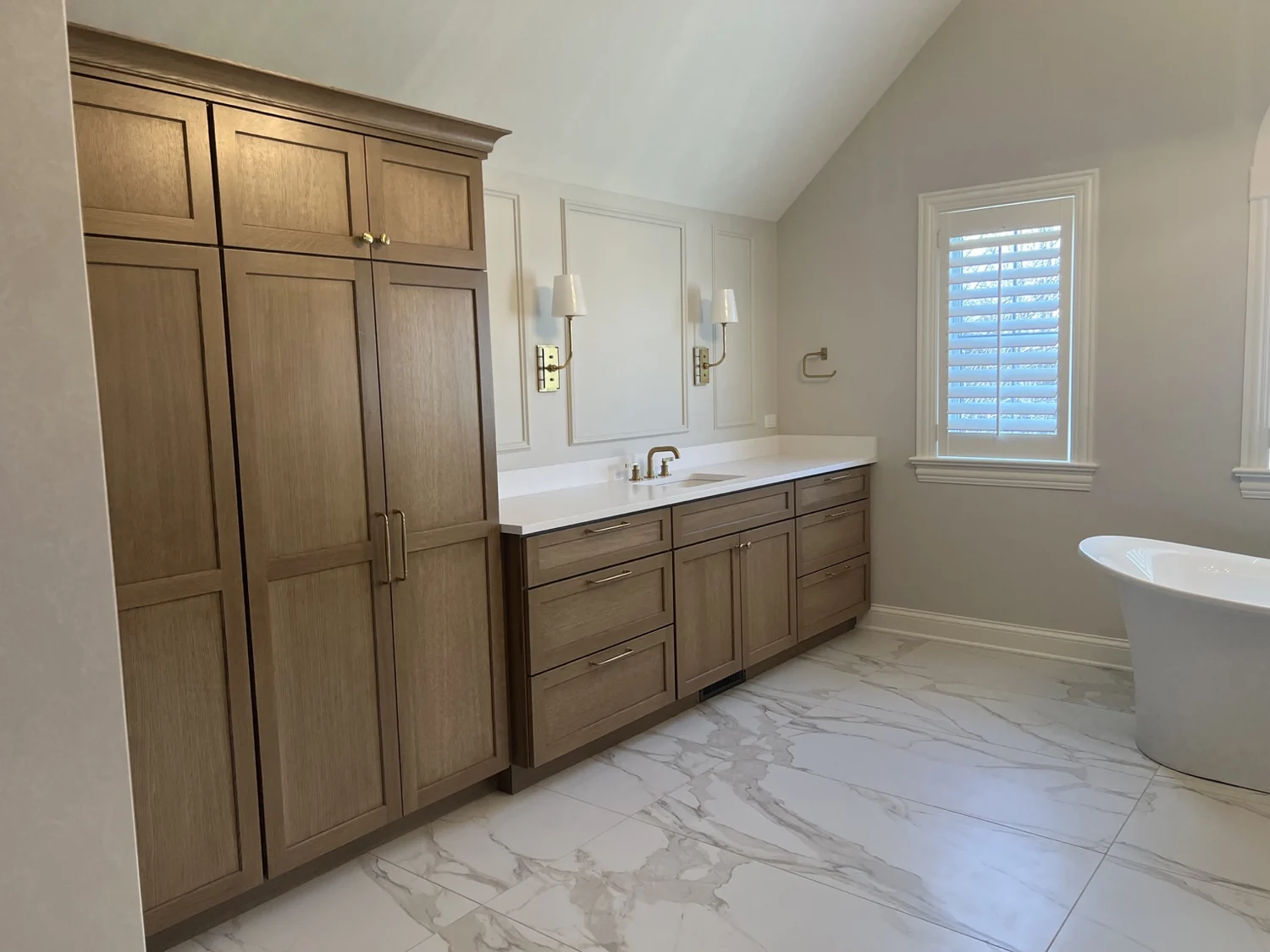 Bathroom with warm wood vanity cabinetry, tall storage cabinet and freestanding tub