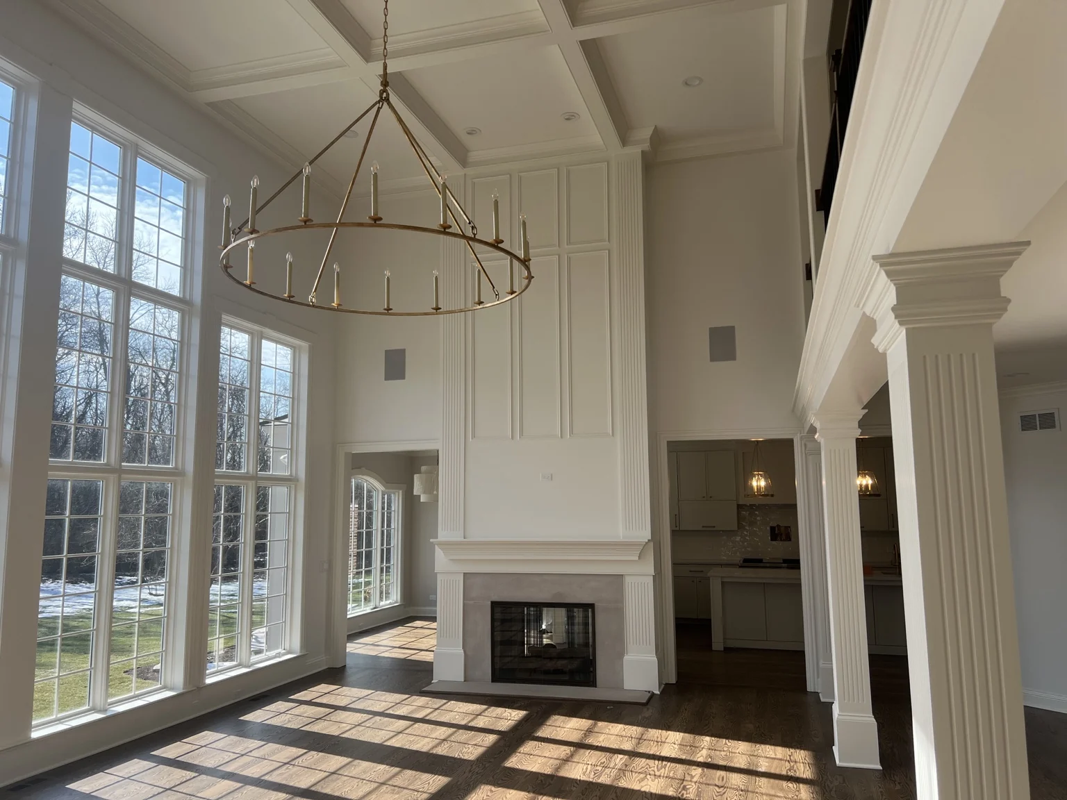 Tall finished living space with fireplace millwork, coffered ceiling, columns and large windows
